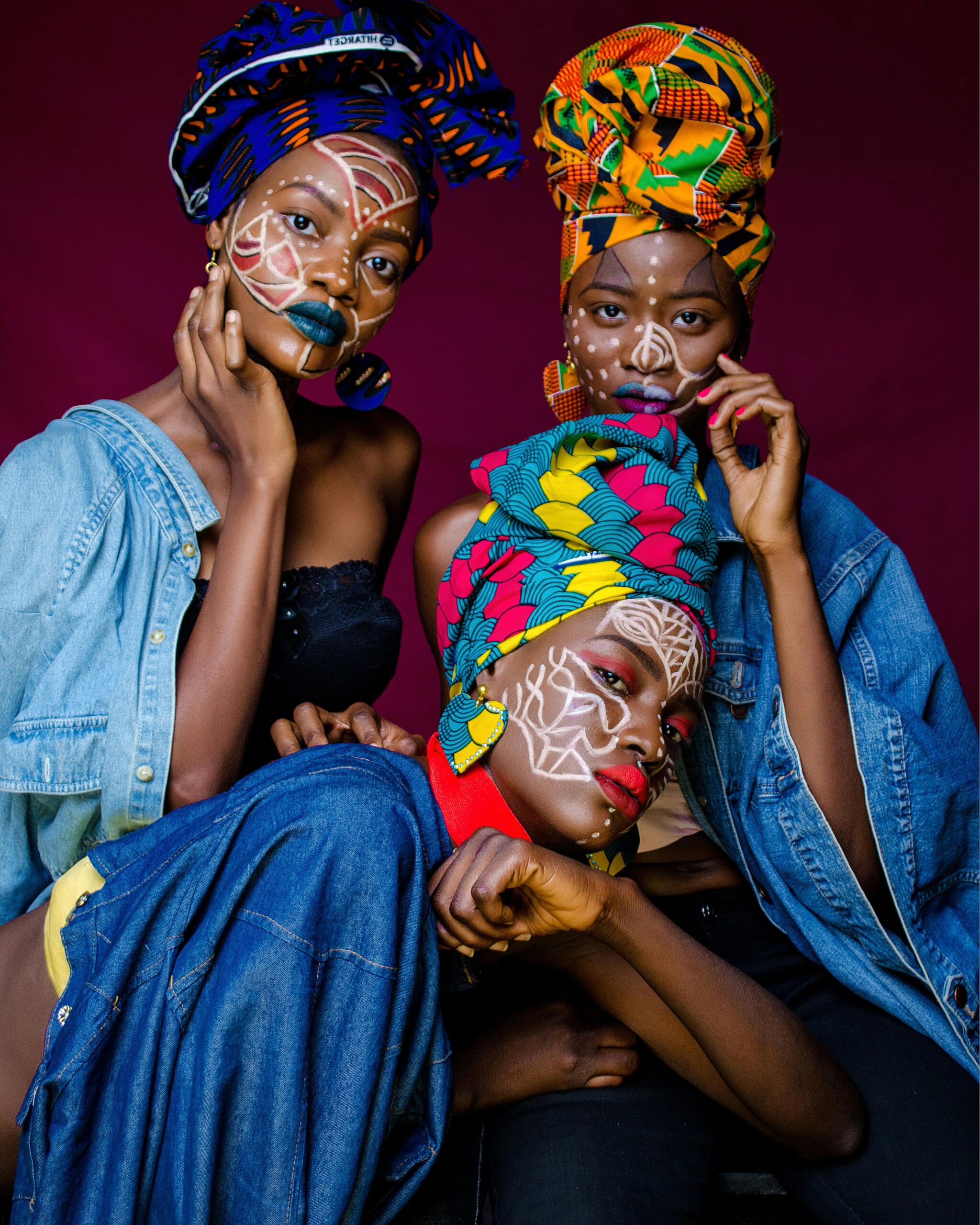 Three women in colorful African outfits with face paint and headdresses celebrating culture.